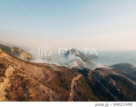 The city on the coast of Montenegro is engulfed in fire. White smoke over the city, the road and the mountains. The city on the coast of Montenegro is engulfed in fire. White smoke over the city, the road and the mountains. 69022490