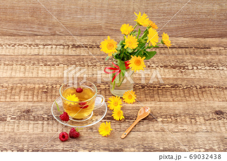Glass cup of green tea with flowers of calendula and fresh raspberries Glass cup of green tea with flowers of calendula and fresh raspberries 69032438