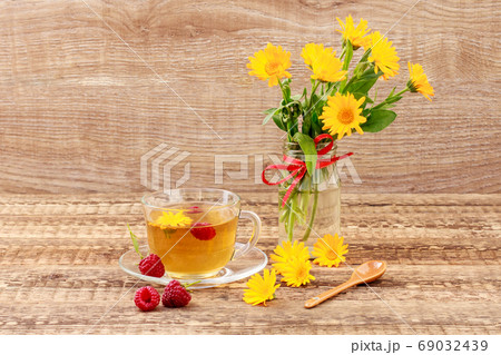 Glass cup of green tea with flowers of calendula and fresh raspberries 69032439