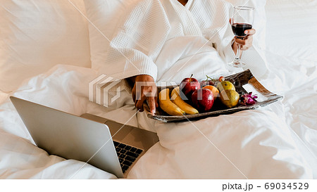 Picture of tourists holding wine, used laptop and eating fruits on the bed, health food concept Picture of tourists holding wine, used laptop and eating fruits on the bed, health food concept 69034529