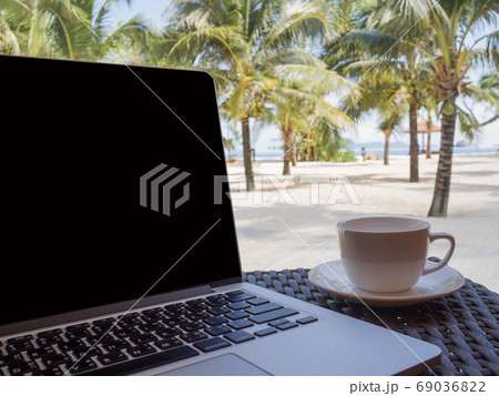 A cup of coffee beside laptop with Coconut tree and sea view, wh A cup of coffee beside laptop with Coconut tree and sea view, wh 69036822