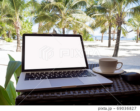 A cup of coffee beside laptop with Coconut tree and sea view, white sand beach background 69036827
