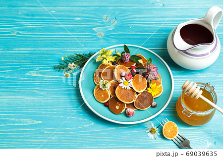 small pancakes with berries on a blue plate. With a jug of syrup and a jar of honey. On a blue wooden background, with space small pancakes with berries on a blue plate. With a jug of syrup and a jar of honey. On a blue wooden background, with space 69039635