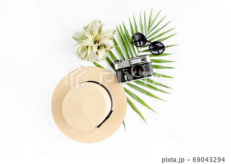 Flat lay traveler accessories on white background with retro camera, straw hat, sunglasses, and tropical palm leaf. Travel concept background. Flat lay traveler accessories on white background with retro camera, straw hat, sunglasses, and tropical palm leaf. Travel concept background. 69043294
