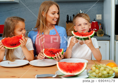 Sweet family, mother and her kids eating watermelon in their kitchen having fun 69044179