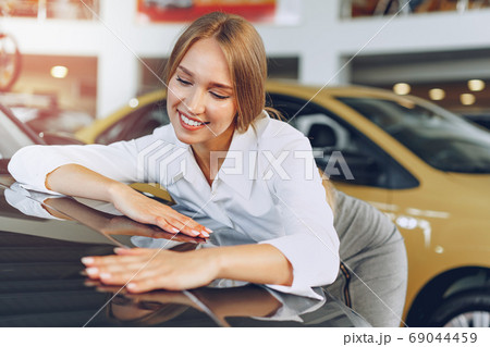 Beautiful young woman touching her new car with pleasure Beautiful young woman touching her new car with pleasure 69044459