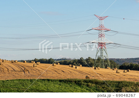 Straw bales on the field near high electricity pylons 69048267