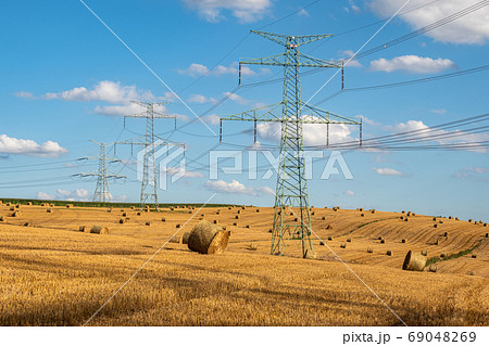 Straw bales on the field near high electricity pylons 69048269