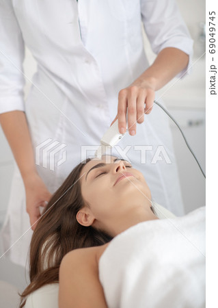 Dark-haired woman lying on the couch while having laser skin treatment in the salon 69049745