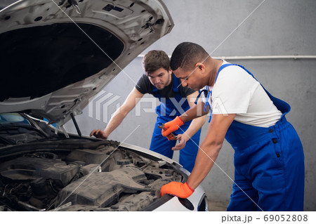 Men inspecting the hood and engine of a vehicle 69052808