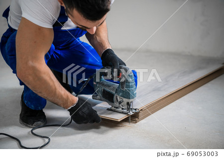 Bearded worker sawing a wooden board with a jigsaw 69053003