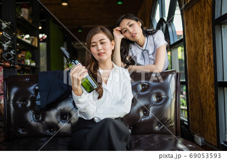 two businesswoman sitting in restaurant, and very drunk, her hand holding bottle of wine. two businesswoman sitting in restaurant, and very drunk, her hand holding bottle of wine. 69053593