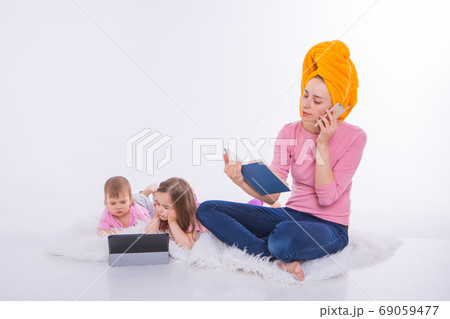 woman with book in her hands is talking on phone. Children watch cartoon on their tablet. mom washed her hair. towel on head. Hobbies and recreation with gadgets. woman with book in her hands is talking on phone. Children watch cartoon on their tablet. mom washed her hair. towel on head. Hobbies and recreation with gadgets. 69059477
