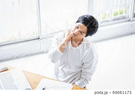 デスクワーク中に片手で肩を押さえる若い男性 69061173