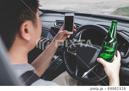 Young asian man drives a car with drunk a bottle of beer and usi Young asian man drives a car with drunk a bottle of beer and usi 69062328