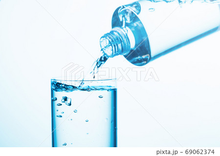 Pouring water from a bottle into glass on a blue background. Pouring water from a bottle into glass on a blue background. 69062374