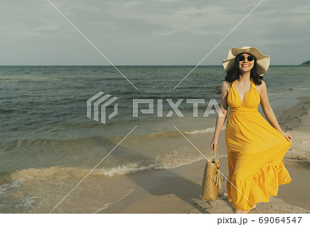 woman in yellow dress walking on the sea beach 69064547