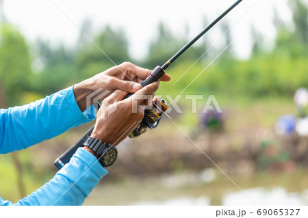 Fishing reel and rod in fisherman hand in a pond 69065327