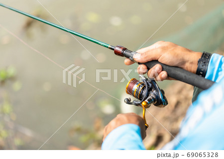 Fishing reel and rod in fisherman hand in a pond 69065328