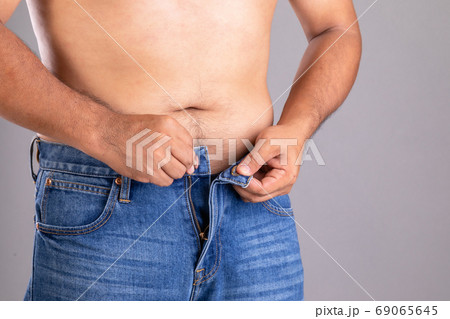Fat man trying to button-up pants studio shot on grey background 69065645