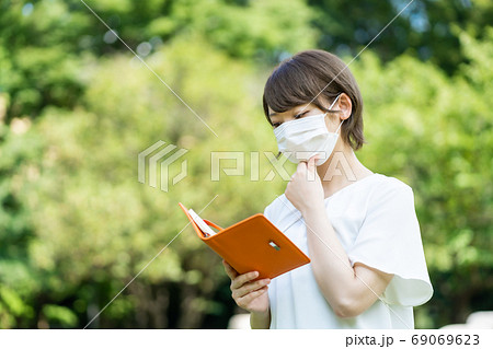 新型コロナ肺炎の中手帳を片手に歩く若い女性 新型コロナ肺炎の中手帳を片手に歩く若い女性 69069623