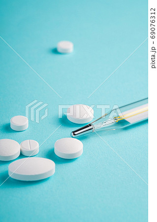 Pills, tablets and analog thermometer on bright blue background Pills, tablets and analog thermometer on bright blue background 69076312