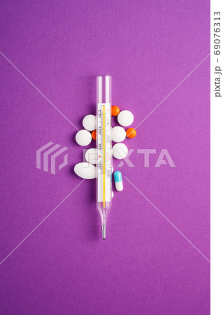 Pills, tablets and analog thermometer on violet background 69076313