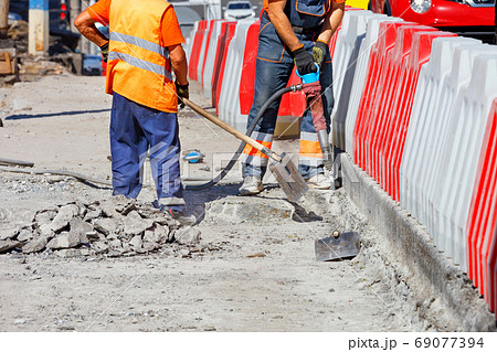 A team of workers cleans some of the concrete with a jackhammer and shovels during road repairs. A team of workers cleans some of the concrete with a jackhammer and shovels during road repairs. 69077394