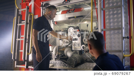 Fireman teaching trainee to use fire engine equipment 69079267