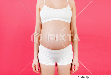 Cropped image of pregnant woman's belly at pink background. Future mom in white underwear. Parenthood concept. Copy space Cropped image of pregnant woman's belly at pink background. Future mom in white underwear. Parenthood concept. Copy space 69079822