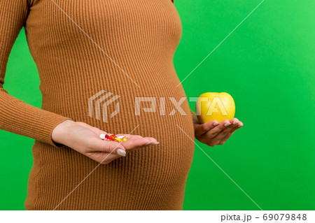 Close up of an apple and a heap of pills in pregnant woman's hands at colorful background with copy space. Making a choice during pregnancy concept Close up of an apple and a heap of pills in pregnant woman's hands at colorful background with copy space. Making a choice during pregnancy concept 69079848