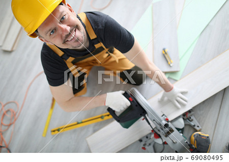 Builder in overalls and hard hat cut laminate on machine in room. 69080495