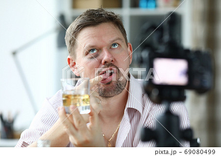Disheveled man hold glass of alcohol in his hand and taste it with his finger. 69080499