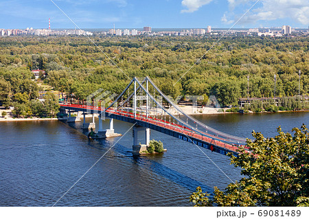 Pedestrian park bridge over the Dnipro river in Kyiv on a sunny summer day. Pedestrian park bridge over the Dnipro river in Kyiv on a sunny summer day. 69081489