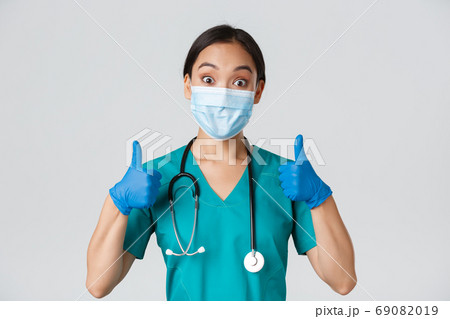 Covid-19, coronavirus disease, healthcare workers concept. Amused smiling asian doctor, physician in medical mask and rubber gloves, showing thumbs-up, approve, praise nice work Covid-19, coronavirus disease, healthcare workers concept. Amused smiling asian doctor, physician in medical mask and rubber gloves, showing thumbs-up, approve, praise nice work 69082019
