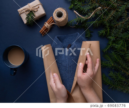 Hands wrapping gift wrapping on blue sweater background Hands wrapping gift wrapping on blue sweater background 69083776