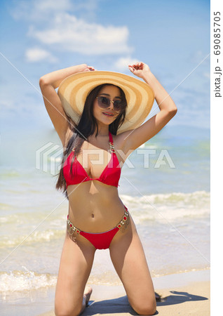 Girl in red bikini with hat & sunglasses relaxing at beach 69085705