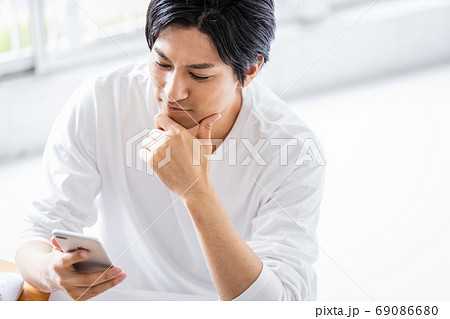 デスクワーク中にスマホ操作をしている若い男性 69086680