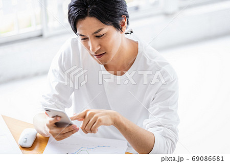 デスクワーク中にスマホ操作をしている若い男性 デスクワーク中にスマホ操作をしている若い男性 69086681