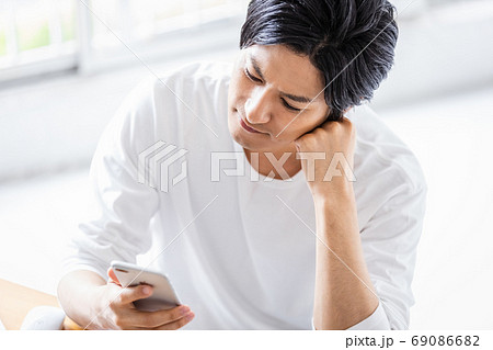 肩肘をついてスマホの画面を見る若い男性 69086682