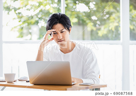 ノートパソコンの画面を見て厳しい表情の若い男性 69087568