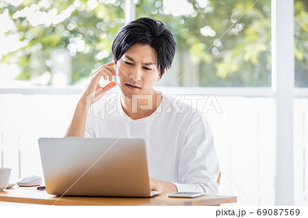 ノートパソコンの画面を見て首をかしげる若い男性 69087569