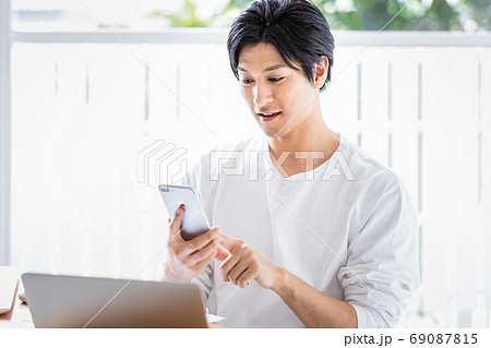 デスクワーク中にスマホを見ている若い男性 69087815