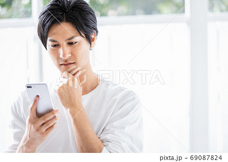 スマホを見て何かを考える若い男性 69087824