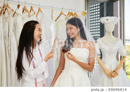 Asian bride trying on wedding dress with female tailor having fun and smiling 69096814