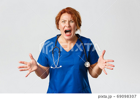 Medicine, healthcare and coronavirus concept. Anxious and frustrated, screaming female doctor, nurse going nuts, shouting, shaking hands, losing temper and feeling mad, standing over grey background Medicine, healthcare and coronavirus concept. Anxious and frustrated, screaming female doctor, nurse going nuts, shouting, shaking hands, losing temper and feeling mad, standing over grey background 69098307