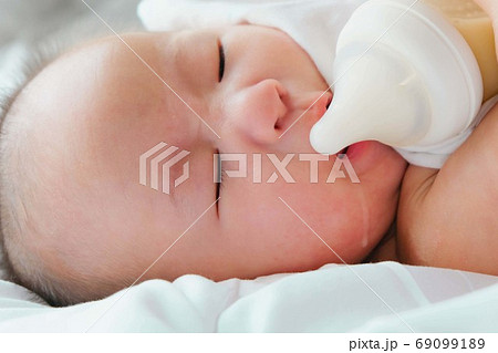 Portrait of a newborn Asian baby on the bed drinks milk from a bottle, Charming black-eyed baby 4 month old lies in bed ,A child resting on a bed Portrait of a newborn Asian baby on the bed drinks milk from a bottle, Charming black-eyed baby 4 month old lies in bed ,A child resting on a bed 69099189
