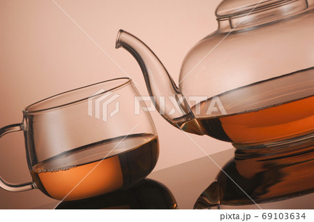 Transparent glass teapot and cup of tea on the reflective surface 69103634