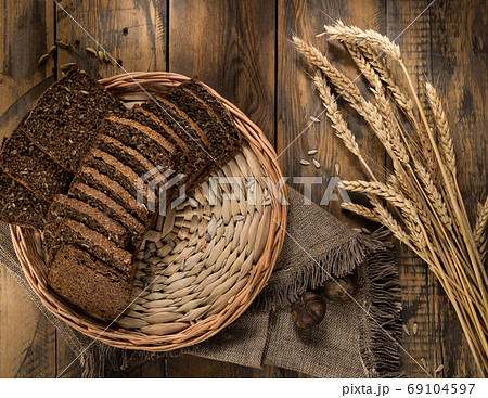 Sliced rye bread in a wicker tray and spikelets on wooden. Top view  69104597