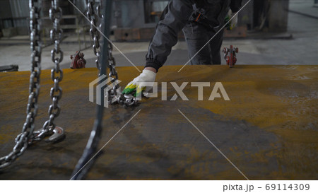 A worker hooks a metal sheet to a crane. Crane chain and hook at an industrial plant. hooks for lifting steel. A worker hooks a metal sheet to a crane. Crane chain and hook at an industrial plant. hooks for lifting steel. 69114309
